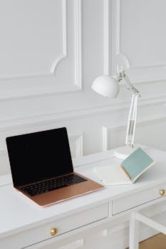 Clean and modern office desk with a laptop, desk lamp, and notebooks in a minimalist setting.